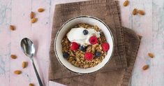 a bowl of cereal with yogurt and berries on top next to a spoon