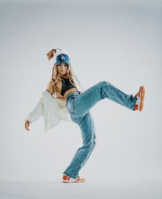 a woman in jeans and a baseball cap is dancing