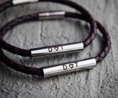 two leather bracelets with silver beads and the word love written on them are sitting on a stone surface