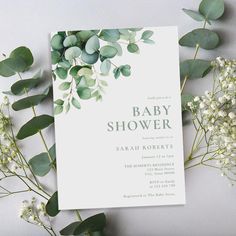 the baby shower is next to some flowers and greenery in front of it's white card