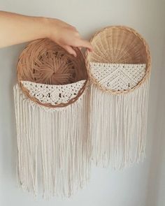 two baskets with white crochet and tassels hanging from the wall next to each other