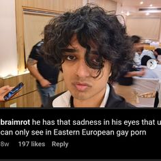 an image of a man with curly hair looking at the camera and holding a cell phone in his hand