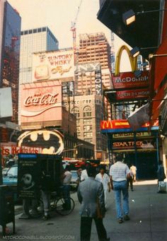 people are walking down the street in front of some tall buildings and neon signs with advertisements on them