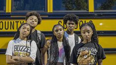 four young people standing in front of a school bus