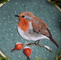 a cross stitch bird sitting on top of a tree branch next to some leaves and berries