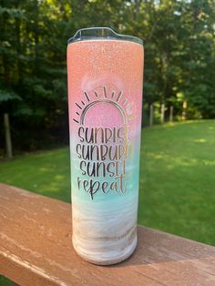 a pink and blue tumbler sitting on top of a wooden table next to trees