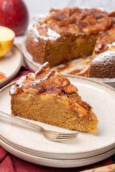 a slice of apple cake on a plate with a fork next to it and an apple in the background