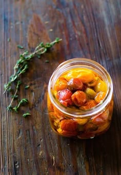 a glass jar filled with pickled tomatoes on top of a wooden table next to a sprig of rosemary