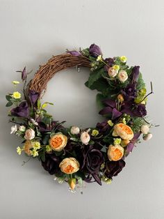 a wreath with flowers and greenery hanging on the wall next to a white wall