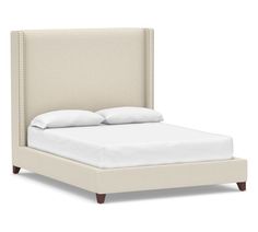 an upholstered bed with white sheets and pillows