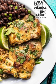 a white plate topped with chicken, beans and avocado next to lime wedges