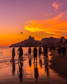 people walking on the beach at sunset with mountains in the backgrounds