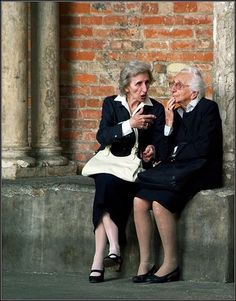 two people sitting on a ledge next to each other and one is holding a cell phone