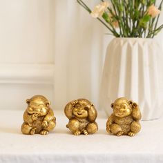 three gold monkey figurines sitting next to a white vase with flowers in it