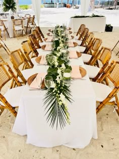 a long table set up with white linens and greenery for an outdoor wedding reception