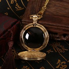 a gold pocket watch with a black stone in the center sits on a table next to an open book