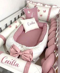 a baby crib with pink and white bedding and pillows on top of it