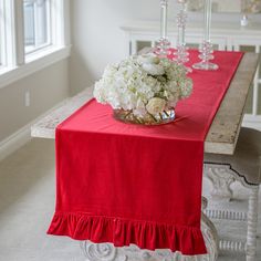 a red table runner with white flowers in a bowl on it and chandelier