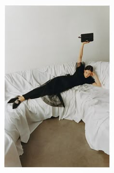 a woman laying on top of a white bed with her legs up in the air