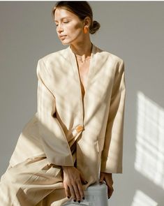 a woman sitting on top of a white chair wearing a tan suit and orange earrings