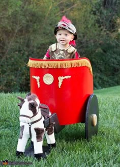 a small child riding in a toy wagon with a dog on the grass next to it