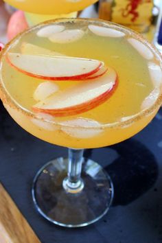 an apple cider sits on a table next to two glasses filled with liquid and sliced apples