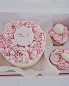 pink cupcakes with white frosting and gold decorations in a cardboard box on a table