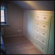 an empty bedroom with white dressers in the corner and a window on the far wall