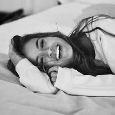 a woman laying on top of a bed next to a white pillow and smiling at the camera