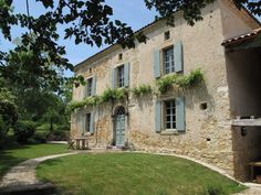 an old stone house with ivy growing on the windows and shutters, in front of a green lawn