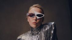 a woman with an eye patch on her face, wearing silver and black clothing in front of a dark background