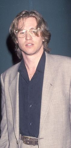 a man with glasses standing in front of a blue wall