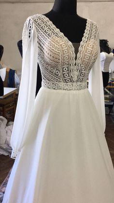 a white wedding dress with sheer sleeves and beading on the neckline, sitting on a mannequin