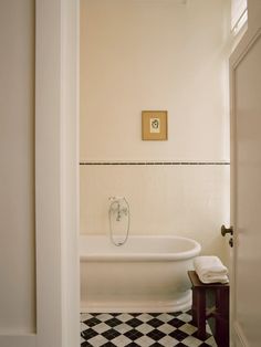 a bathroom with a checkered floor and white bathtub next to a wooden bench