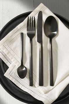 a black plate topped with silverware on top of a white napkin