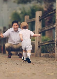 a little boy running next to a man in white shirt and black shoes with his hand out