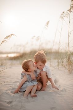 two little boys playing in the sand at the beach with sea oats behind them