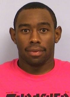 the man is wearing a pink shirt and posing for a mug shot in front of a white wall