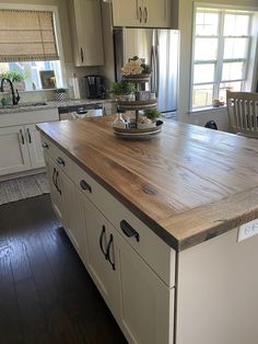 a large kitchen island in the middle of a wooden floored area with white cabinets