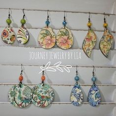 a group of earrings hanging from hooks on a white wall with the words journey jewelry by la written above them