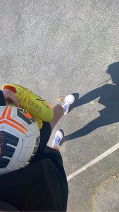 a person holding a soccer ball in their right hand and wearing a yellow shirt with an orange stripe on it