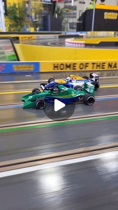 two green race cars driving down a track in front of a yellow sign that says home of the nation