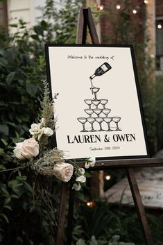 a sign that has some wine glasses on it with flowers in the foreground and lights behind it