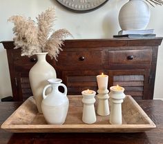 white vases and candles sit on a tray in front of a clock