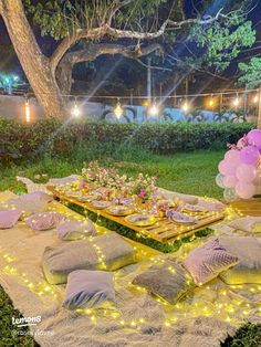 a table set up for a party with pink and purple balloons on it, surrounded by greenery