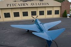 a blue model airplane sitting in front of a building with a sign that says pittcarn aviation