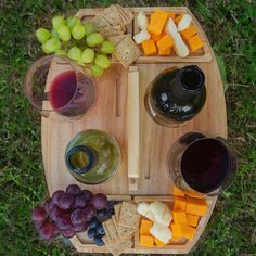 a wooden platter filled with cheese, grapes and crackers next to two glasses of wine