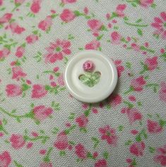 a white button sitting on top of a pink and green flowered table cloth with flowers