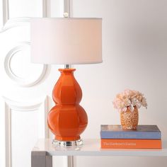 an orange lamp sitting on top of a white table next to a book and flower vase