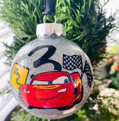 a christmas ornament hanging from a tree with cars painted on it's side